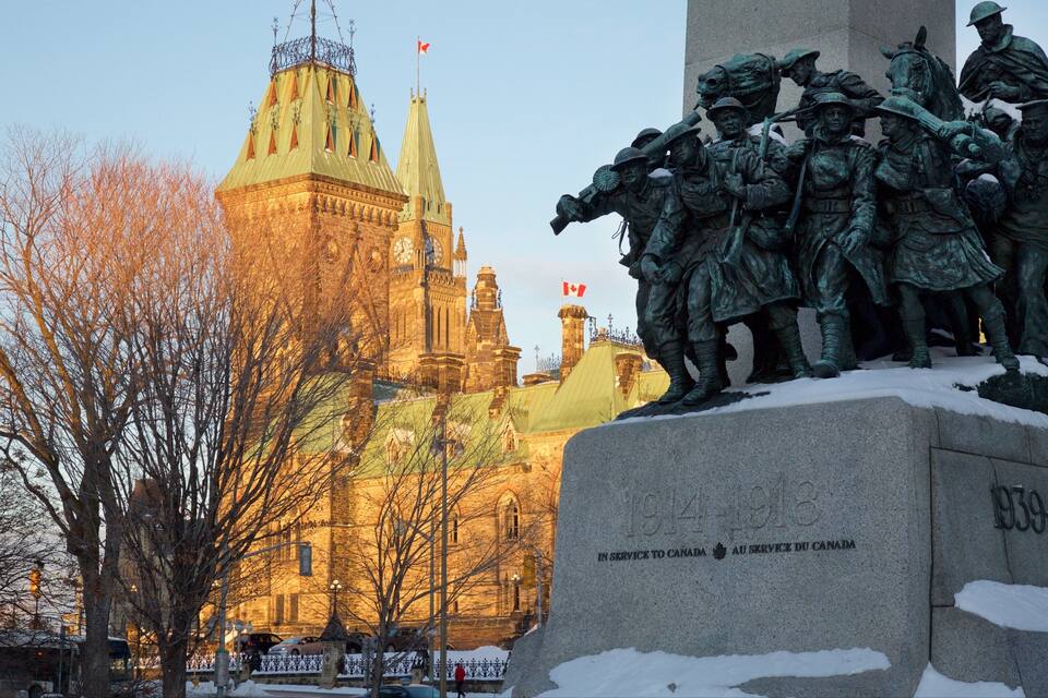 A statue of soldiers, a clock tower, and a building with a Canadian flag.