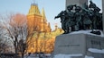 A statue of soldiers, a clock tower, and a building with a Canadian flag.