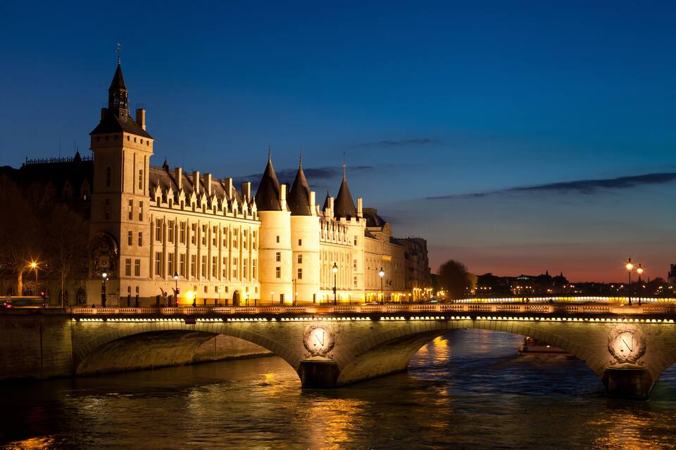 Un edificio histórico con una torre de reloj y un puente con relojes iluminados.