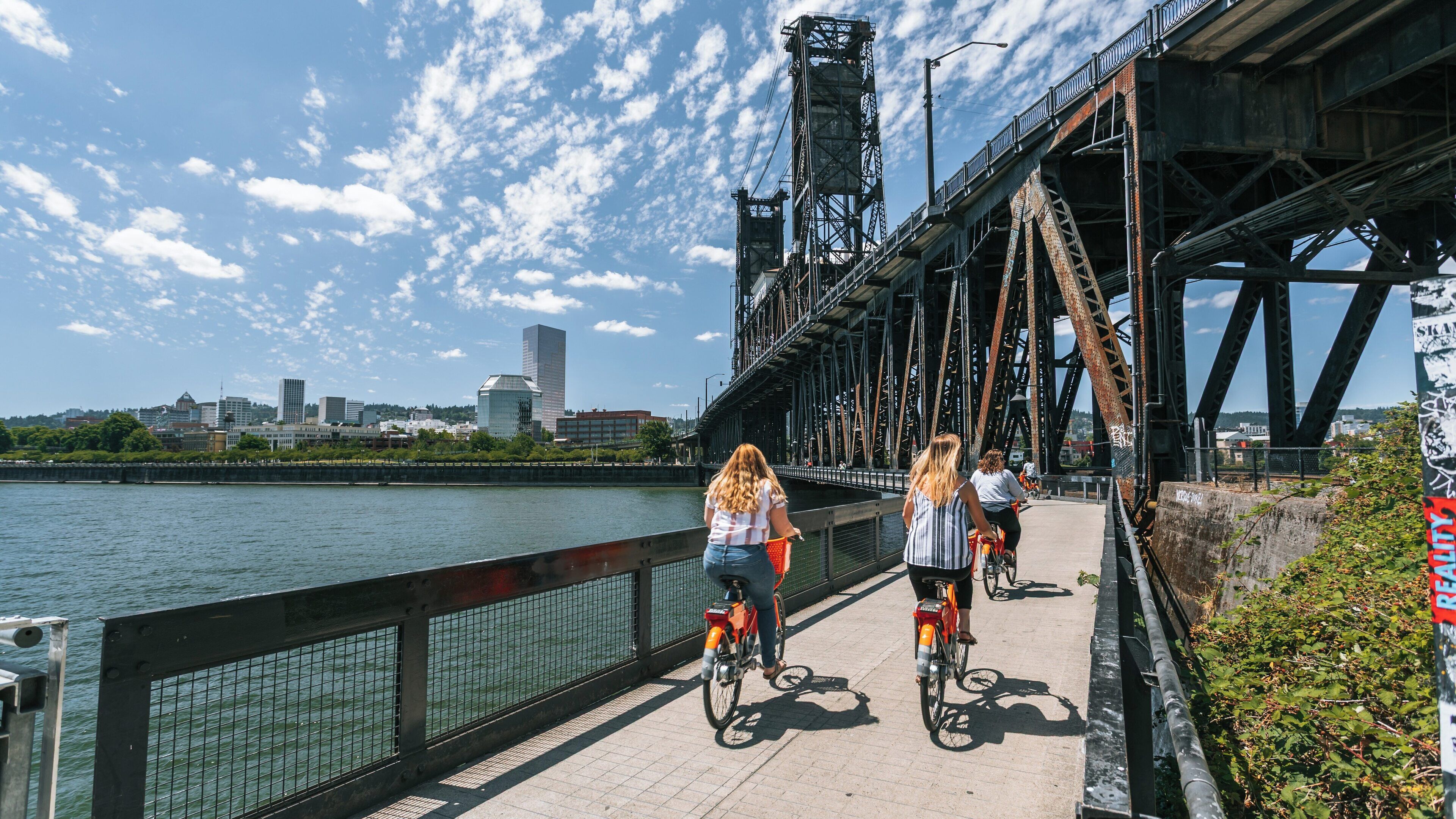 Steel Bridge in Lloyd District showcases cycling enthusiasts enjoying a sunny day in Portland, Oregon near the Willamette River with urban skyline views