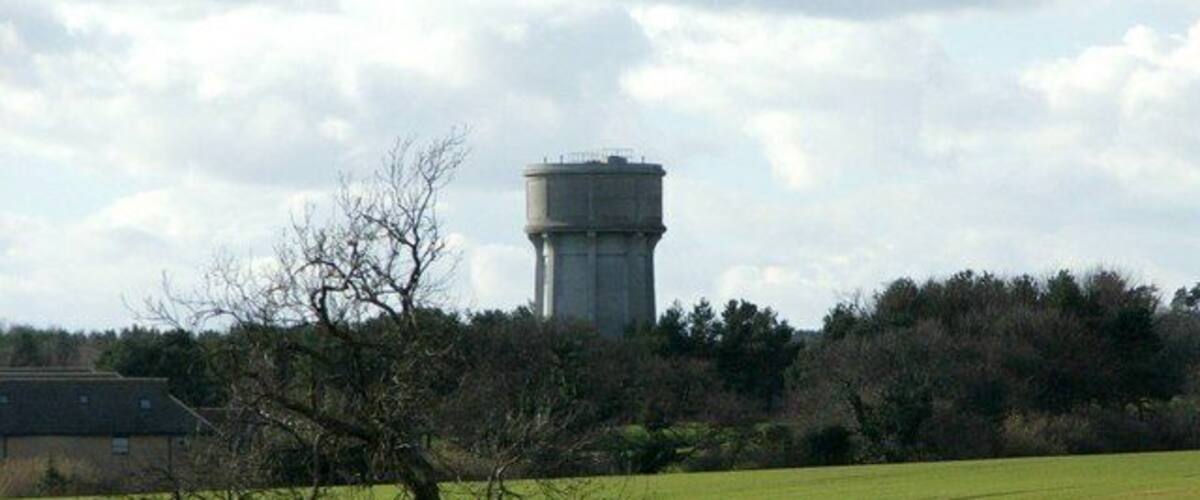 A water tower, a field, and a tree in a rural landscape.