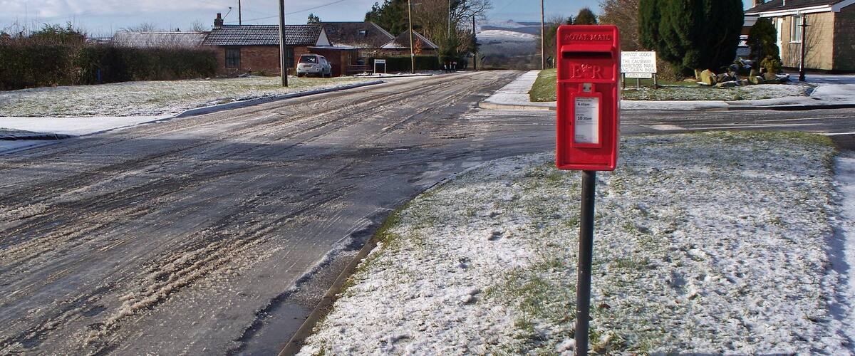 A rural road with a red post box on the right side.