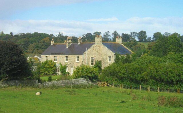 A stone house with a sloped roof, surrounded by lush greenery and trees.