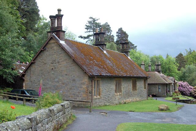 A stone building with a moss-covered roof, surrounded by greenery and a stone wall.