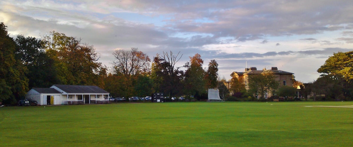 A grassy field with a white building and a large house in the background.