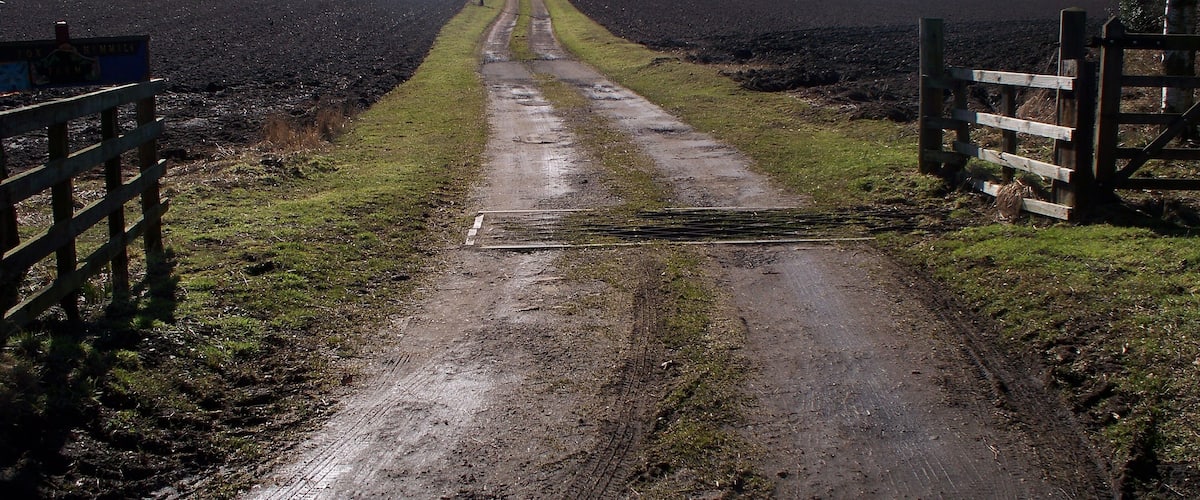 A muddy rural road with a wooden gate on the left and a wooden fence on the right.