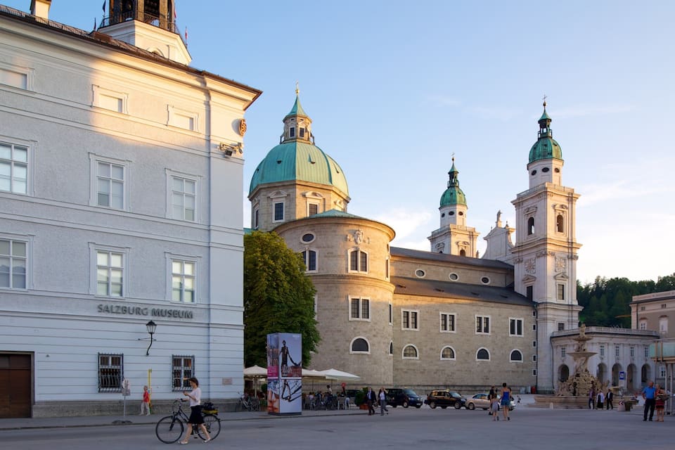 Het Salzburg Museum en een historisch kerkgebouw met groene koepels en torens.