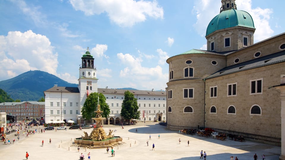 A historic square with a fountain, a clock tower, and a building with a dome.