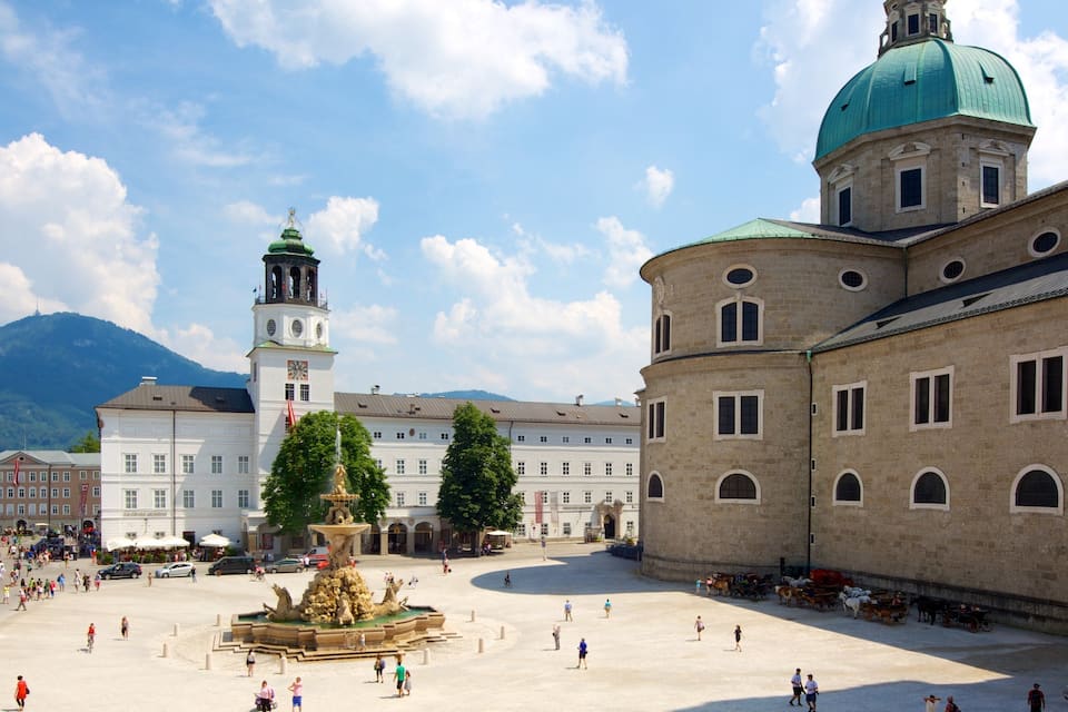 A historic square with a fountain, a clock tower, and a building with a dome.