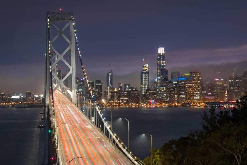A nighttime cityscape with a prominent bridge and illuminated skyscrapers.