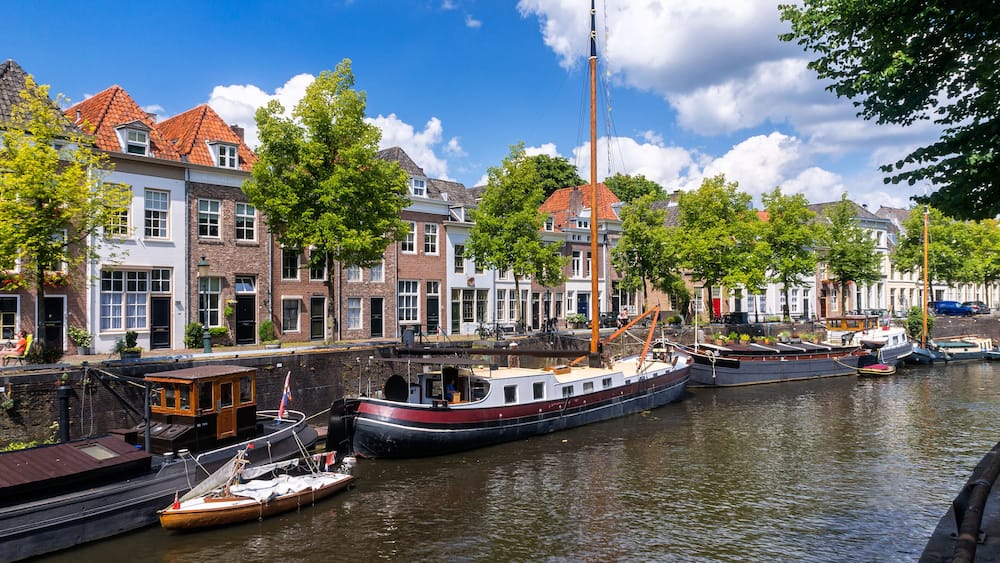 Un canal bordé de bateaux, de bâtiments historiques et d’arbres.