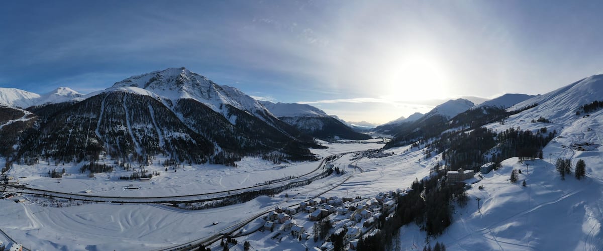 A snow-covered mountain landscape with a ski resort, a winding road, and a clear sky.