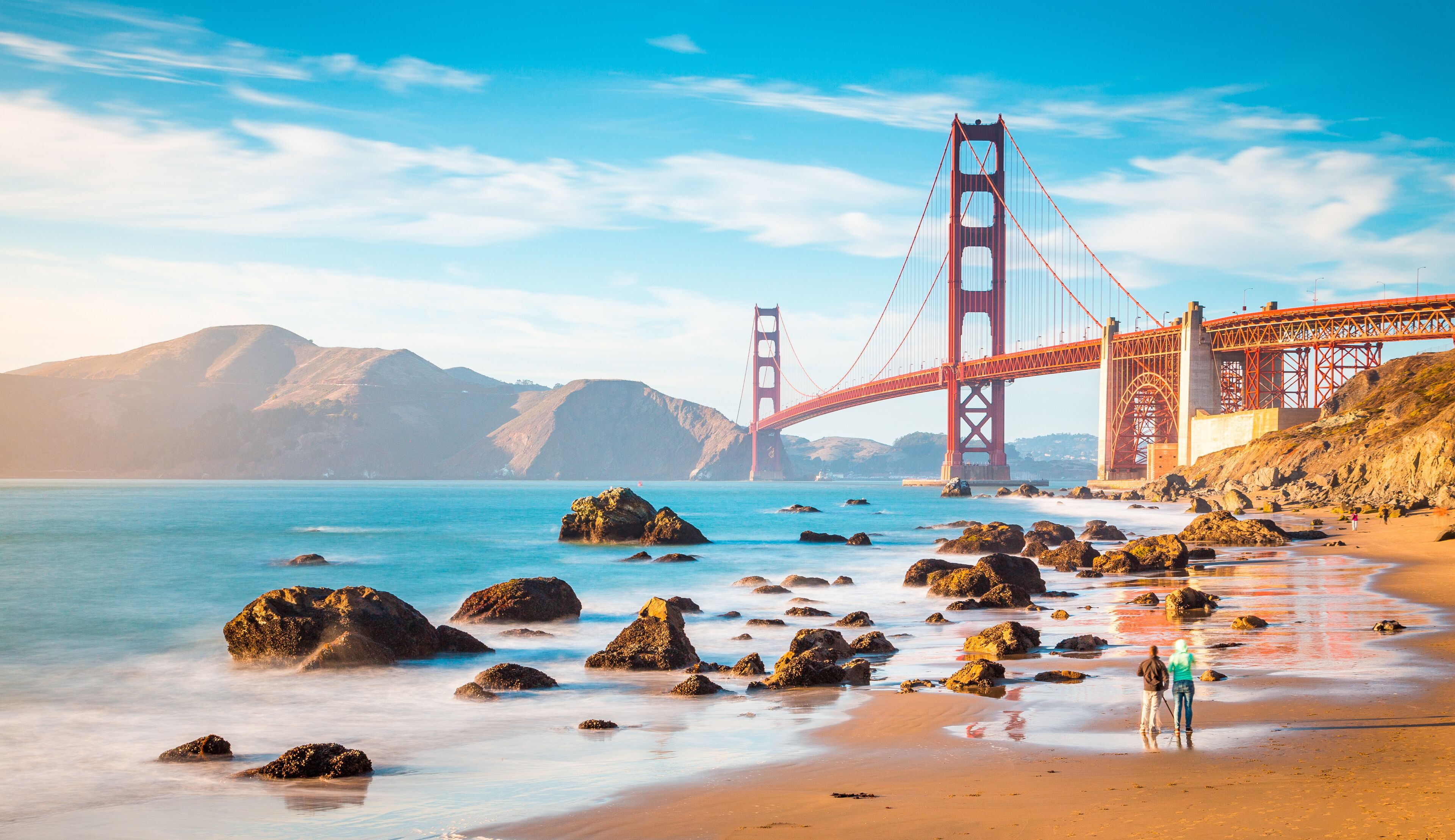Die Golden Gate Bridge, eine Hängebrücke, mit einem Strand und einer felsigen Küste im Vordergrund.