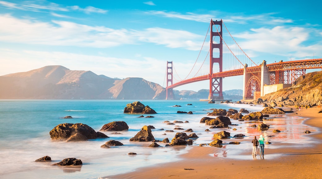 Die Golden Gate Bridge, eine Hängebrücke, mit einem Strand und einer felsigen Küste im Vordergrund.