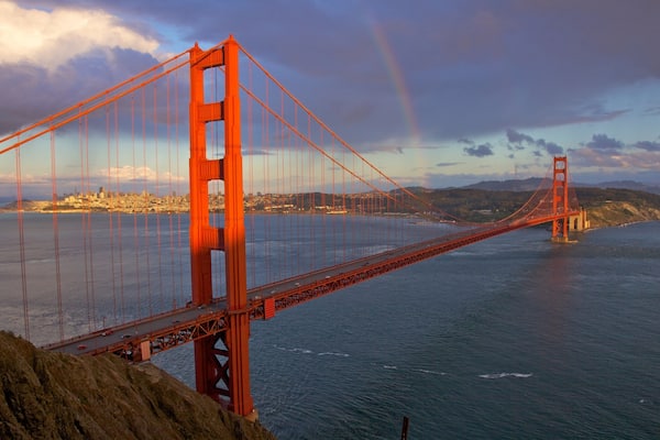 Golden Gate Bridge spans the bay in California under a dramatic sky with a hint of rainbow in the distance