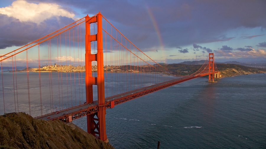 Golden Gate Bridge spans the bay in California under a dramatic sky with a hint of rainbow in the distance