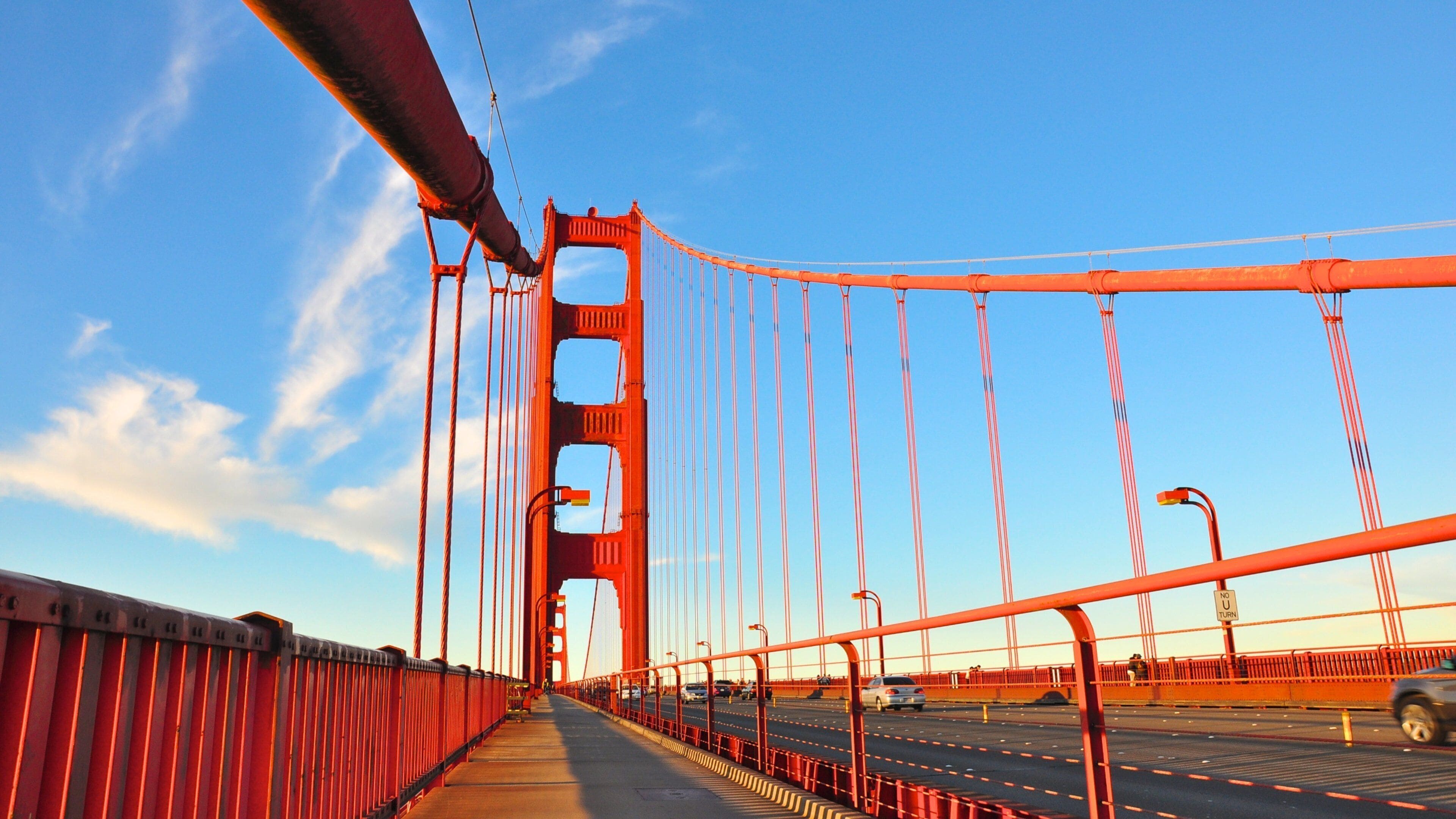 Golden Gate Bridge stretches over the bay in bright blue skies with vibrant architecture and bustling traffic in California