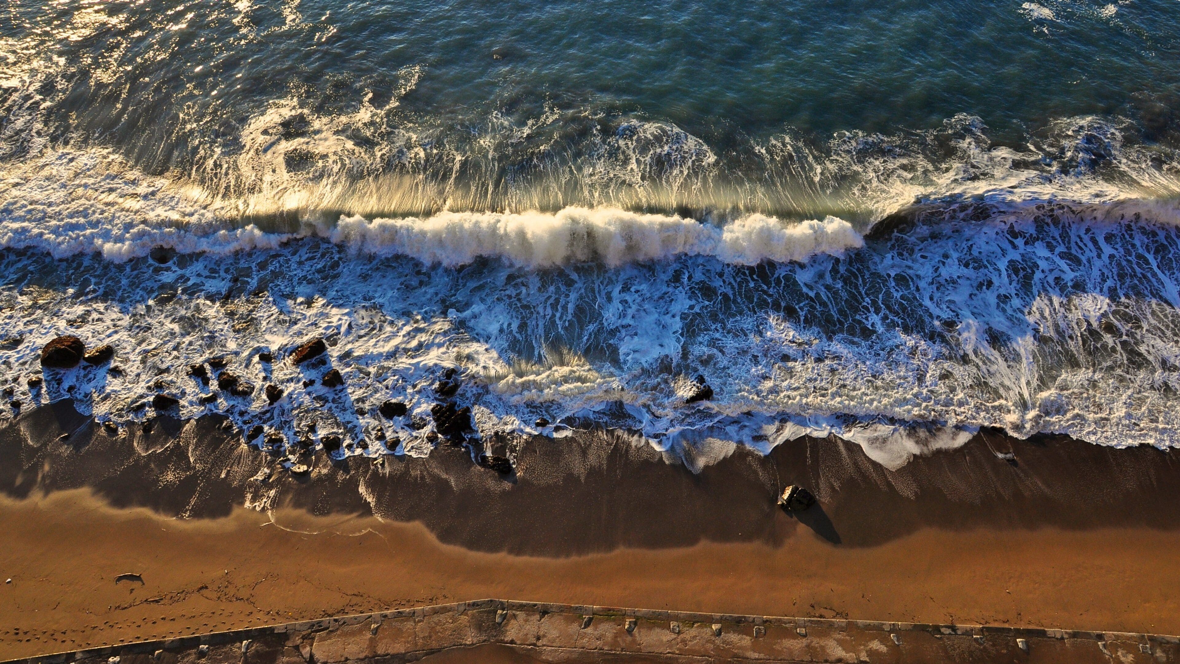 A beach with waves crashing onto the shore and a concrete barrier.