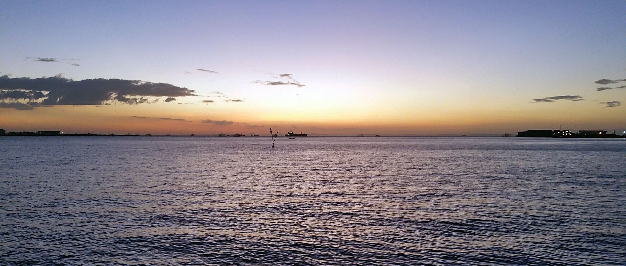 A sunset over a calm sea with distant boats and a clear sky.