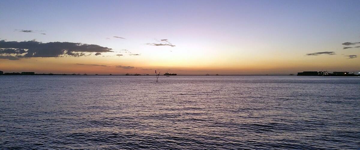 A sunset over a calm sea with distant boats and a clear sky.
