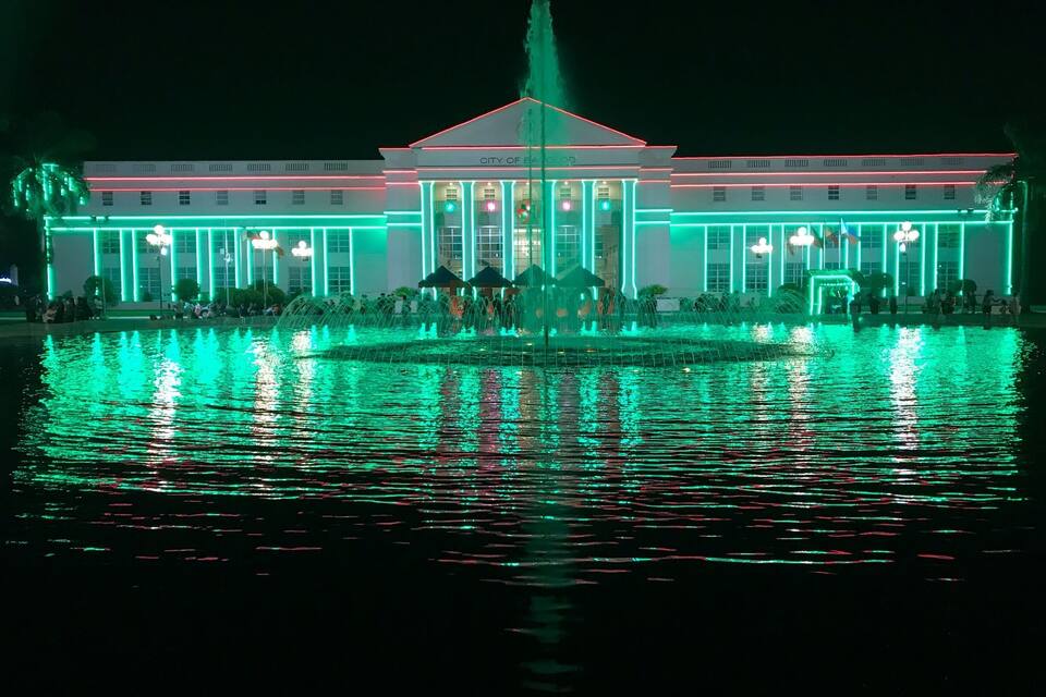 A brightly lit building with a fountain in front, reflecting the lights on the water.