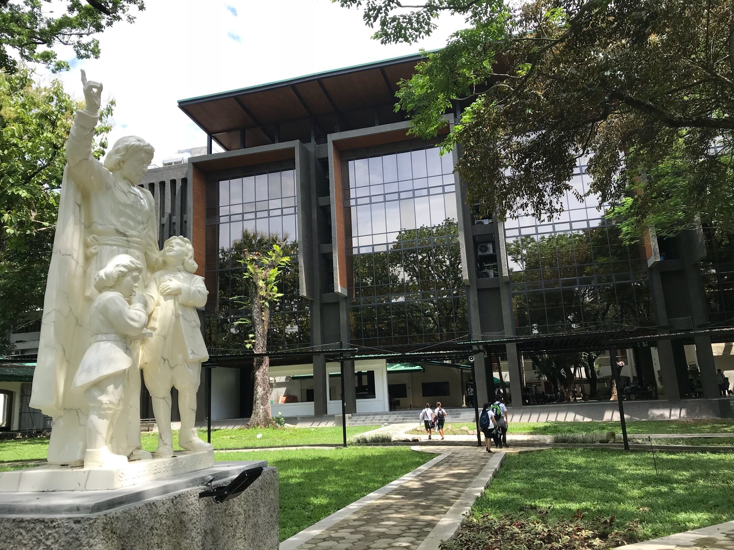 A statue of a historical figure in a park with a modern building in the background.