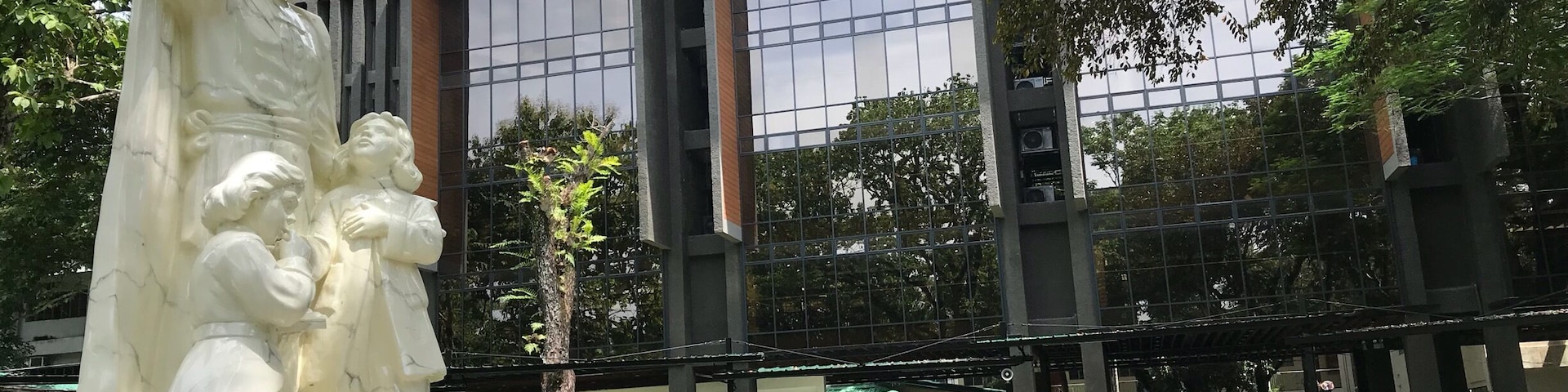 A statue of a historical figure in a park with a modern building in the background.