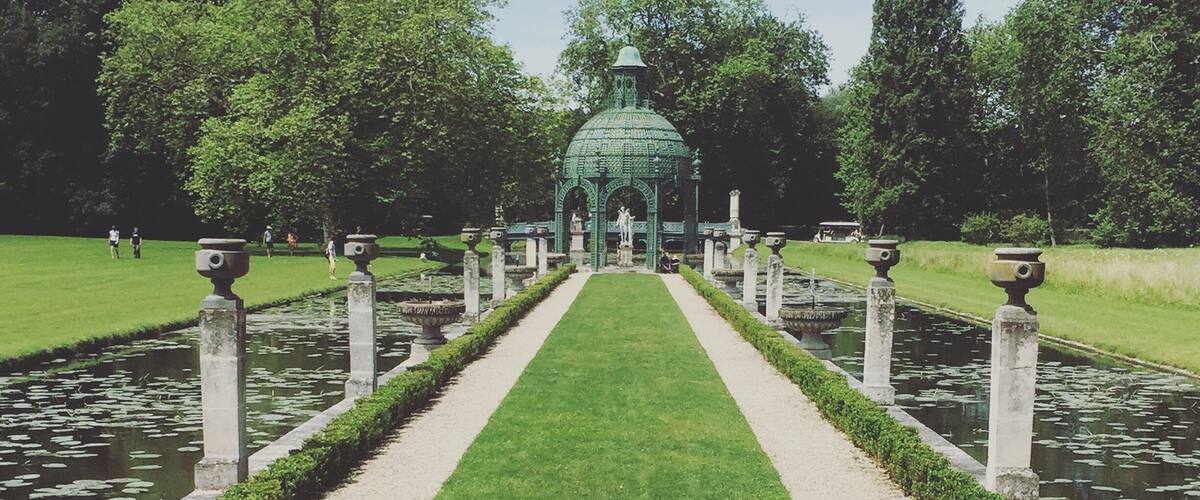 A formal garden with a central pathway, water features, and a green glass structure.