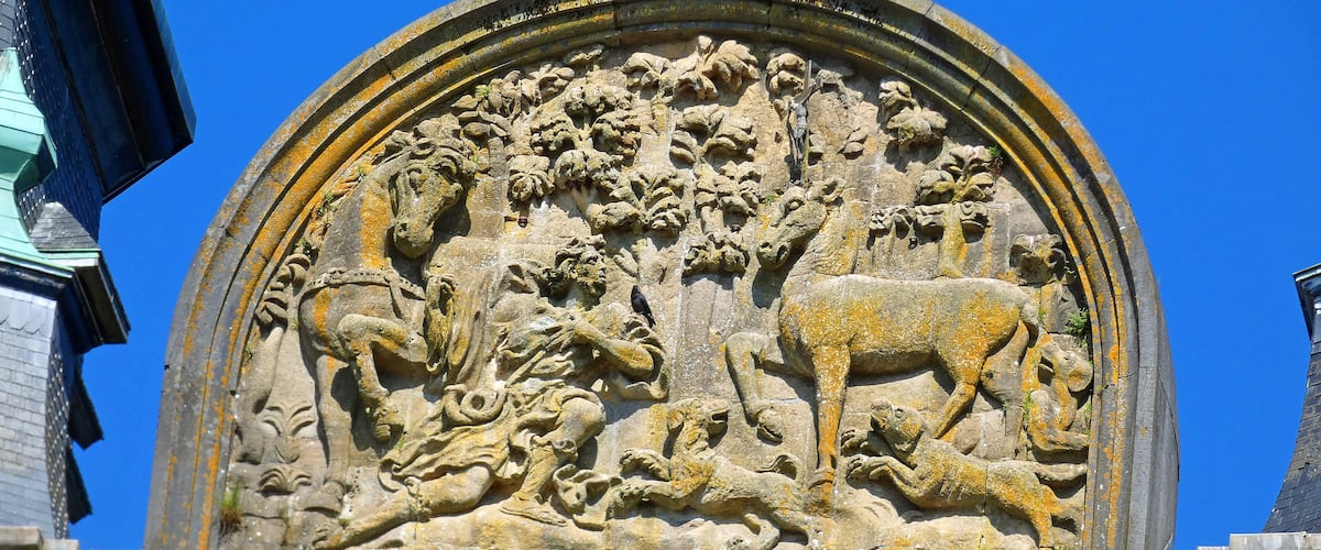 A detailed stone relief sculpture with a lion and a calf, surrounded by foliage and a human figure.