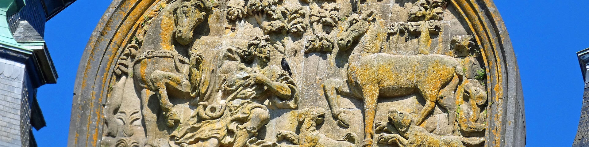 A detailed stone relief sculpture with a lion and a calf, surrounded by foliage and a human figure.