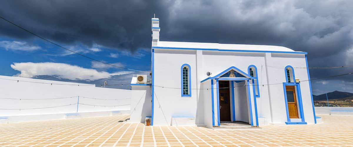 A white church with blue trim and a tiled roof under a cloudy sky.