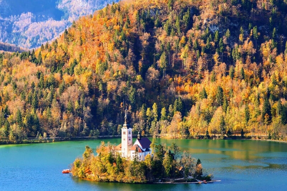 Un lago rodeado de árboles con colores otoñales y una iglesia en una pequeña isla.