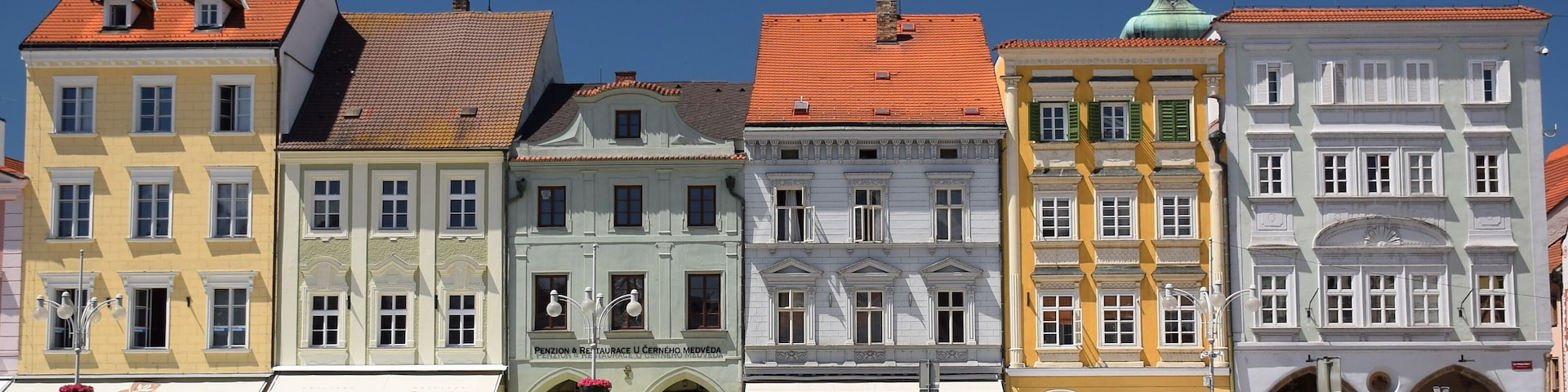 Una hilera de edificios históricos coloridos con tejados de tejas rojas y una plaza adoquinada.