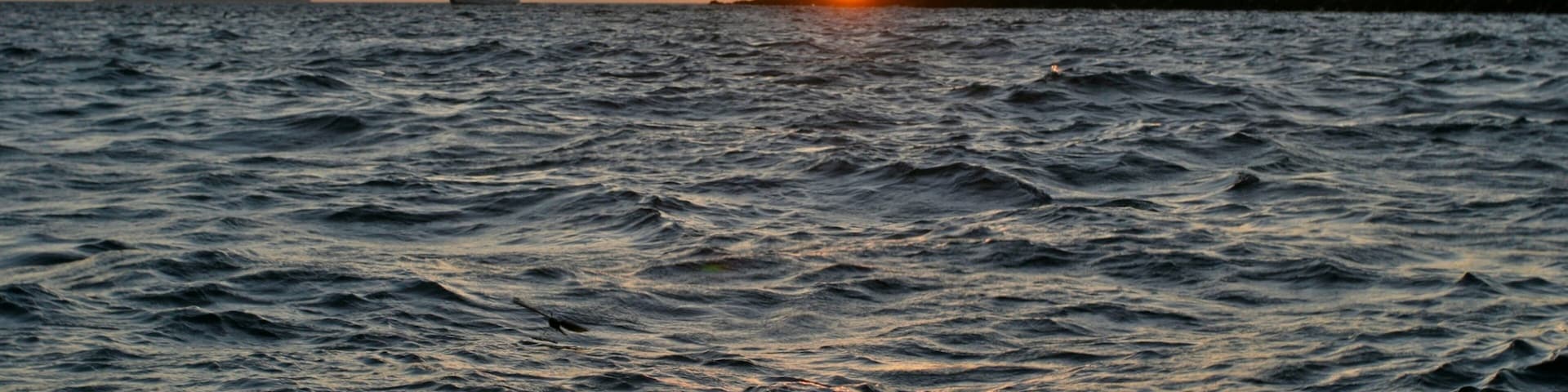 Ein Sonnenuntergang über einem aufgewühlten Meer mit einem Segelboot in der Ferne.