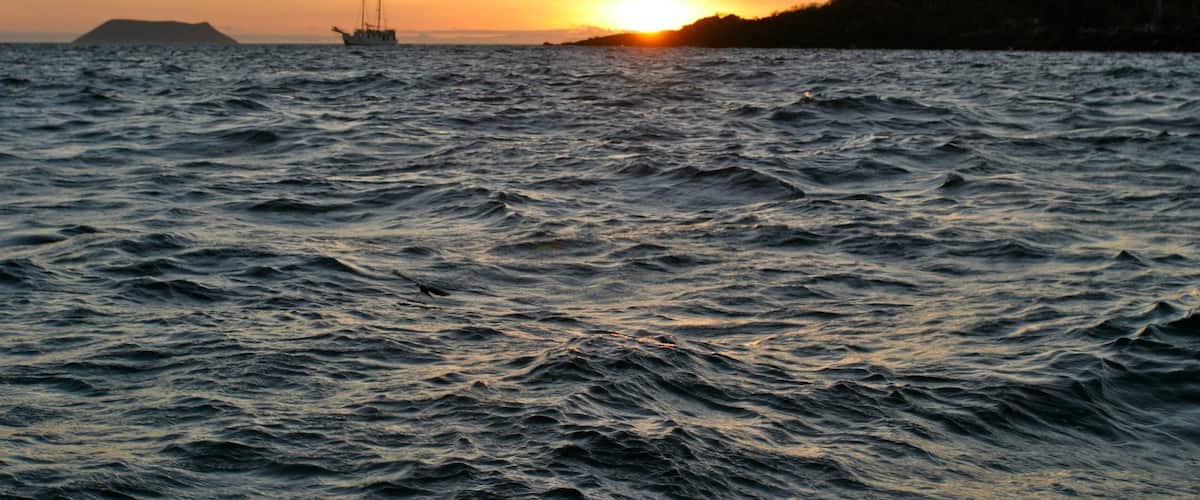 A sunset over a choppy sea with a sailboat in the distance.