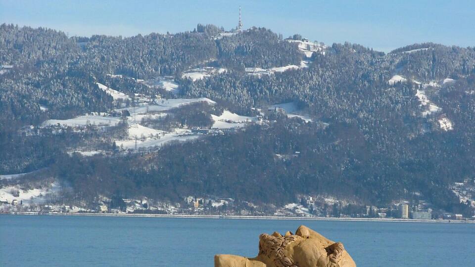 A snow-covered mountain range with a clear blue sky and a large rock in the foreground.