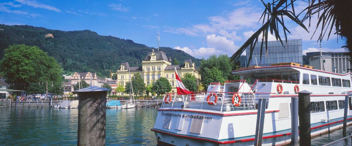 A boat docked at a pier with a mountain and buildings in the background.