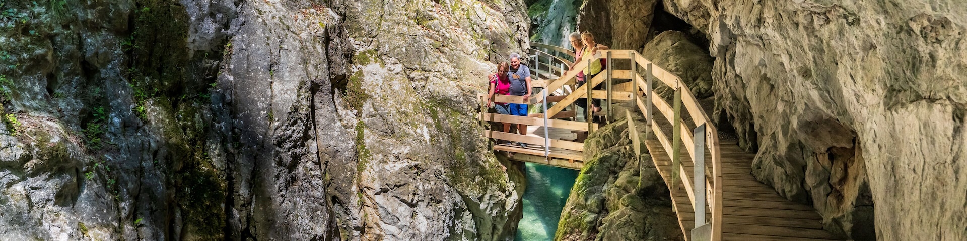 A wooden bridge over a narrow canyon with clear water.