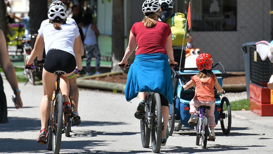 A group of cyclists on a paved street with trees and buildings in the background.