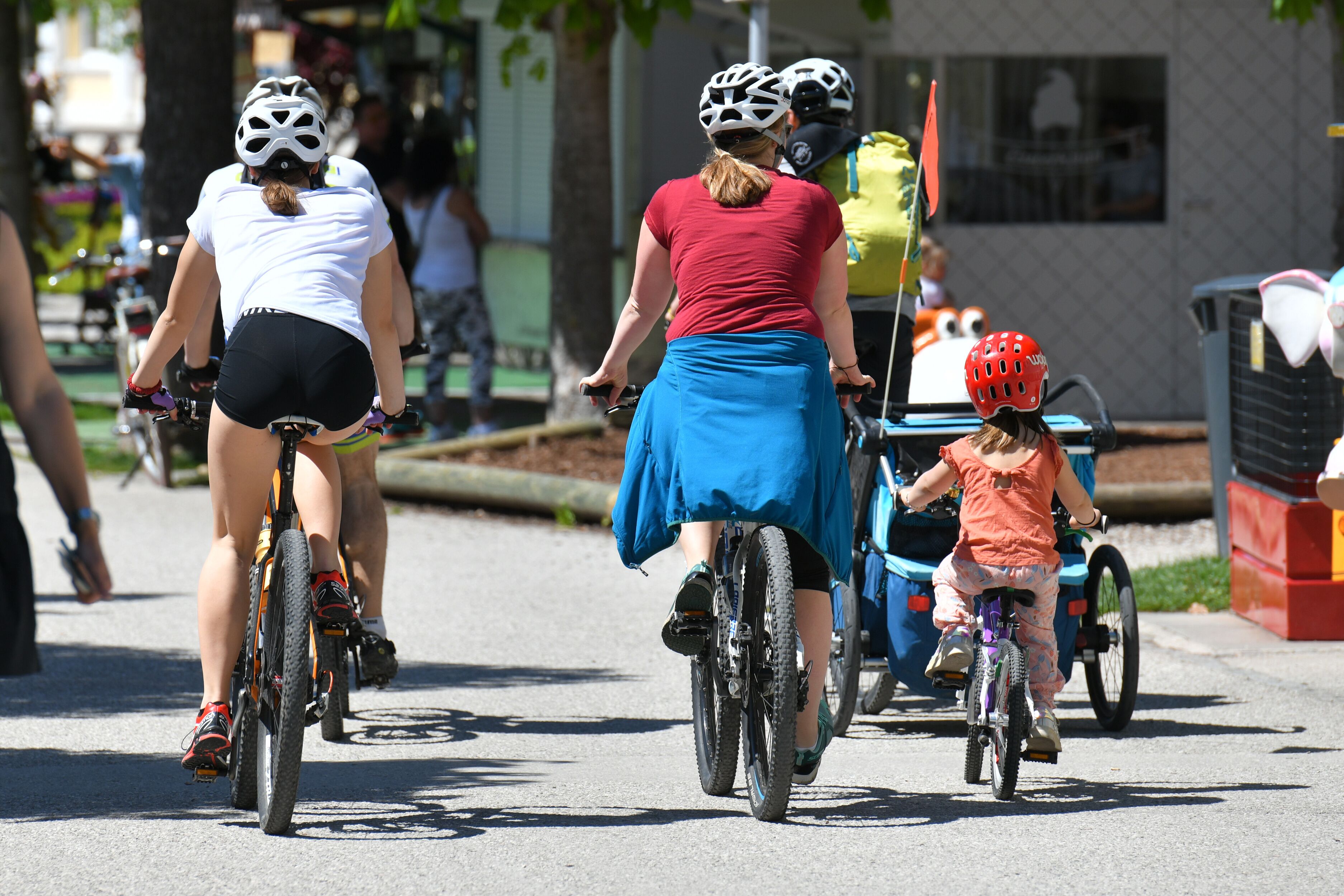 A group of cyclists on a paved street with trees and buildings in the background.