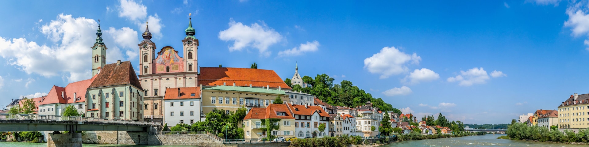A river with a bridge, historic buildings, and a church with two towers.