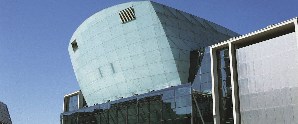 A modern building with a curved glass facade and a large, angular structure on top.