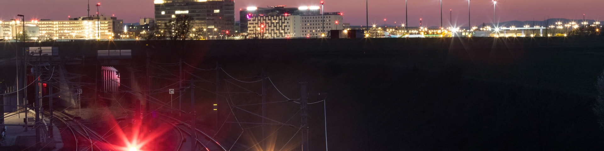 An airplane landing at night near a city with illuminated buildings and a prominent tower.