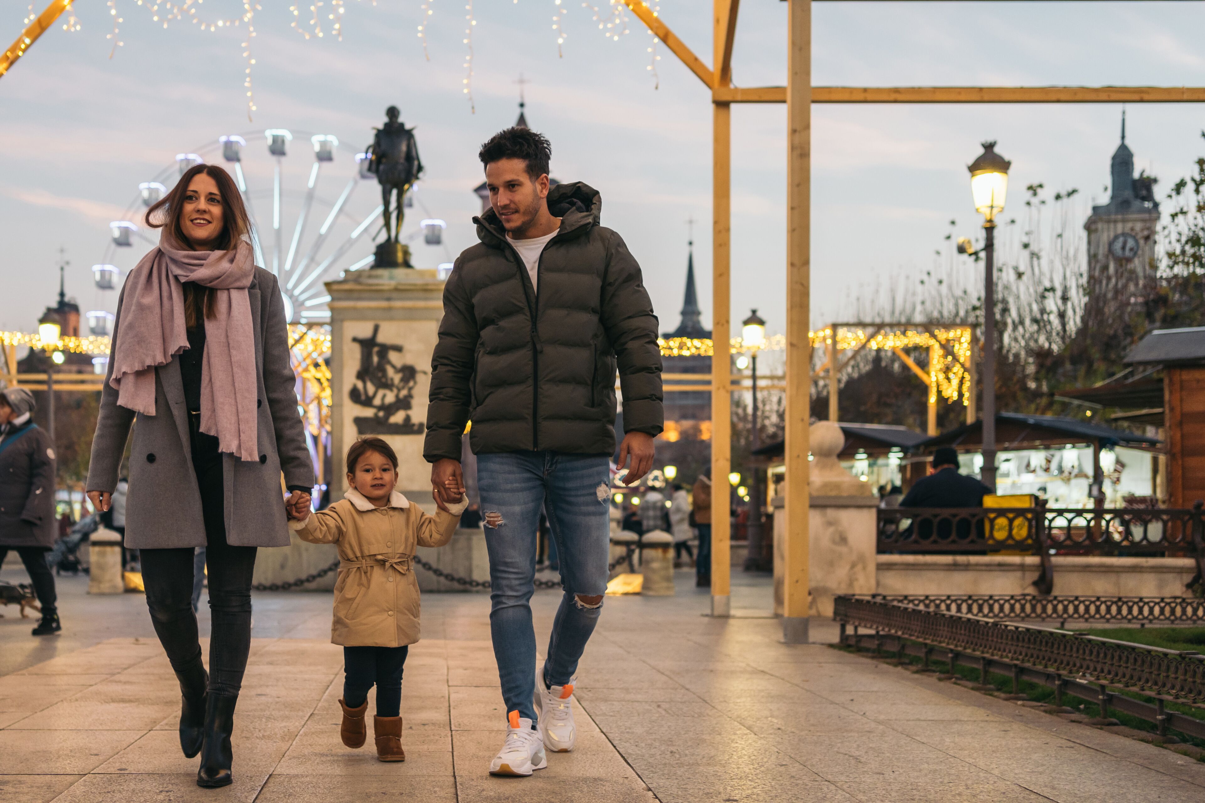 A family walking on a paved path with a Ferris wheel and a clock tower in the background.