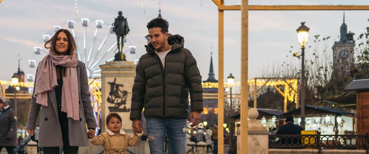 A family walking on a paved path with a Ferris wheel and a clock tower in the background.