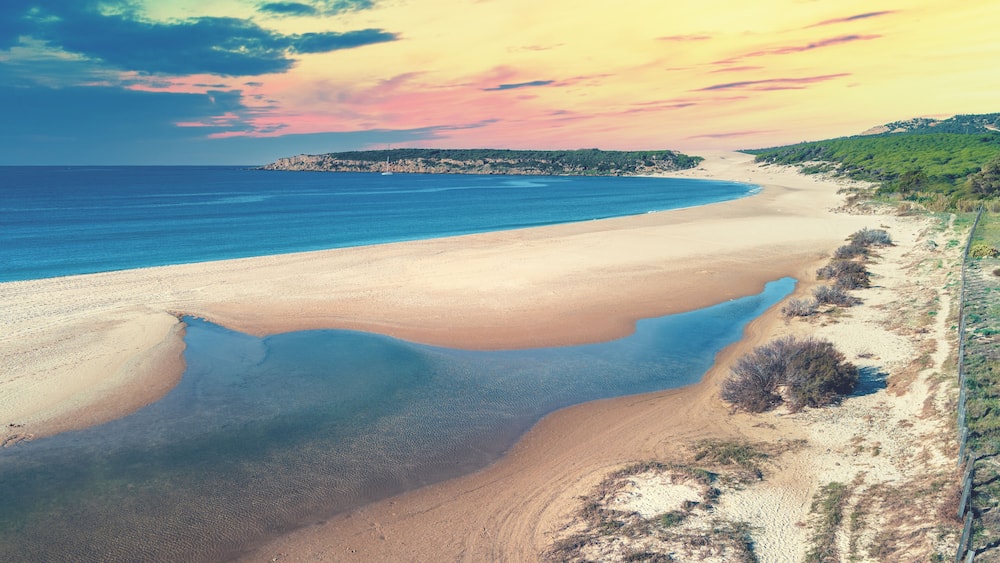 Un paysage cĂŽtier avec une plage, des eaux dâun bleu limpide et une cĂŽte rocheuse qui sâĂ©tend au loin.