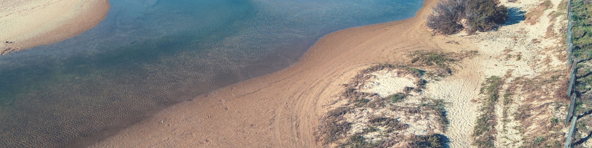 A coastal landscape with a sandy beach, a clear blue sea, and a distant rocky outcrop.