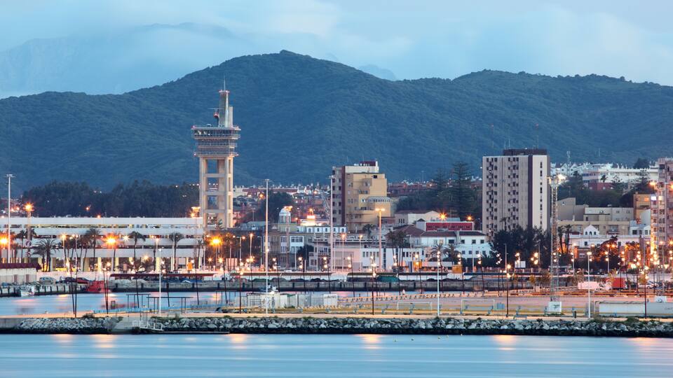 A coastal cityscape with a prominent tower, a calm harbor, and a mountain in the background.