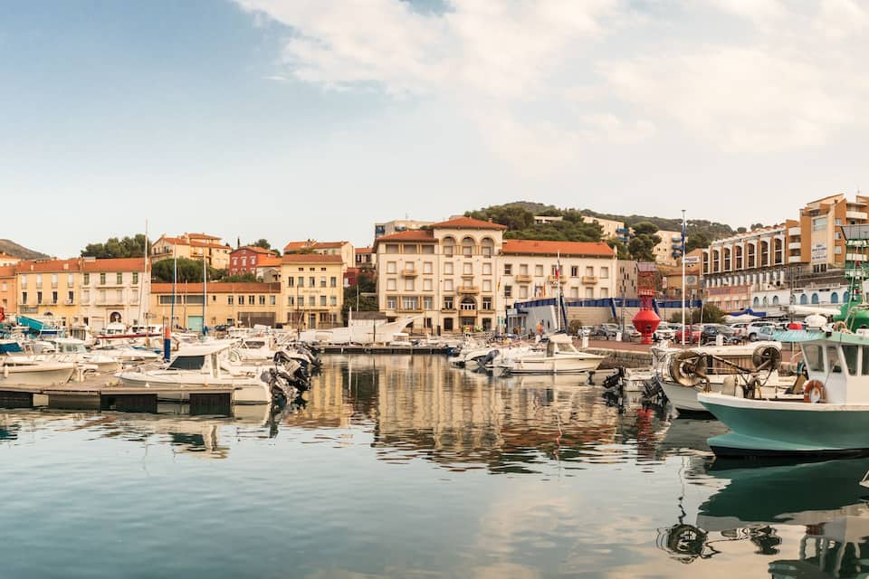 Un port de plaisance avec des bateaux amarrés, une tour de l’horloge et des bâtiments le long de la promenade.