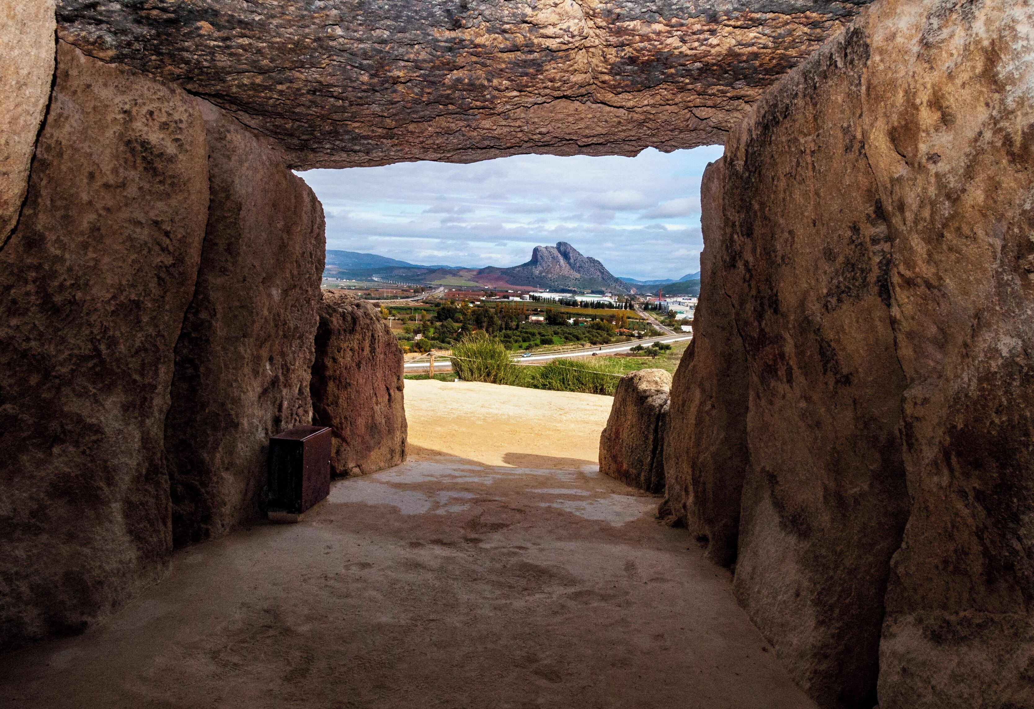 A cave opening with a view of a mountain and a town in the distance.